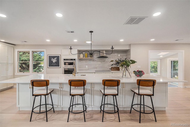 kitchen featuring a breakfast bar, decorative light fixtures, a large island, stainless steel double oven, and light wood-type flooring