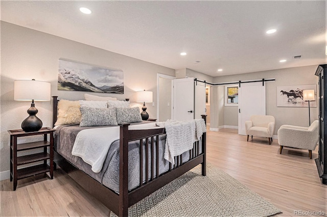 bedroom with a barn door and light hardwood / wood-style floors