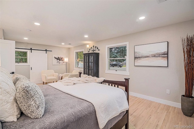 bedroom featuring multiple windows, a barn door, and light hardwood / wood-style flooring