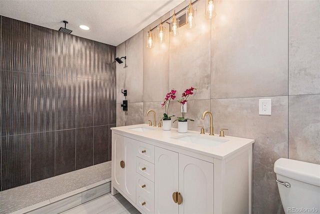 bathroom with tile walls, tiled shower, vanity, a textured ceiling, and toilet