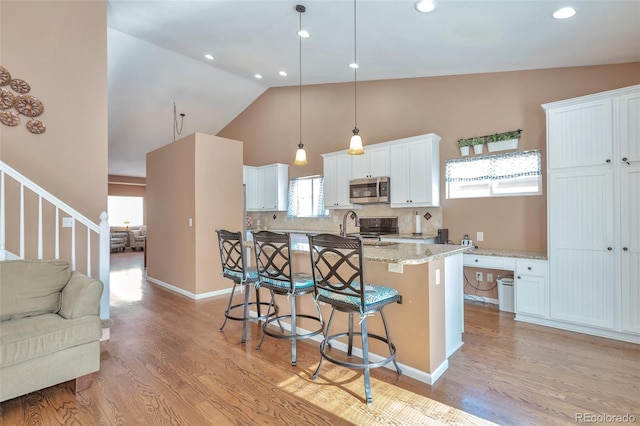 kitchen with a center island with sink, light wood-style flooring, stainless steel microwave, a kitchen breakfast bar, and white cabinetry