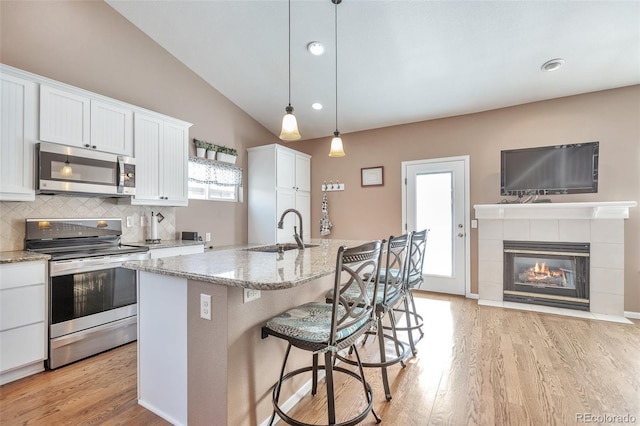 kitchen featuring vaulted ceiling, light stone counters, appliances with stainless steel finishes, white cabinets, and a sink