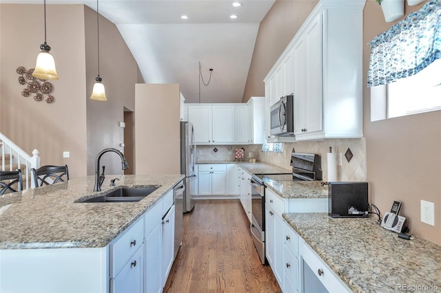 kitchen with a kitchen island with sink, a sink, wood finished floors, white cabinetry, and appliances with stainless steel finishes