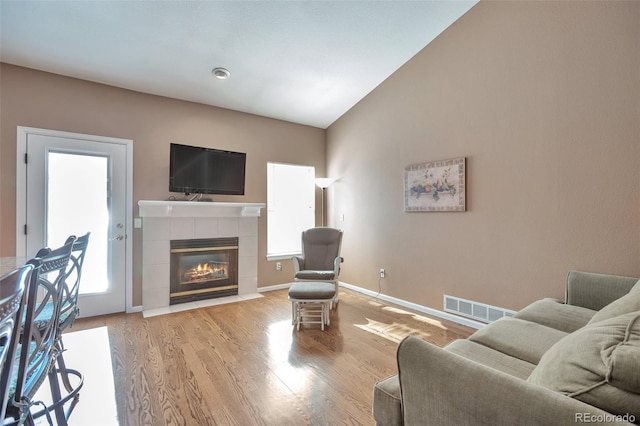 living room with visible vents, baseboards, a tiled fireplace, lofted ceiling, and wood finished floors