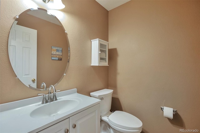 half bath with vanity, toilet, and a textured wall