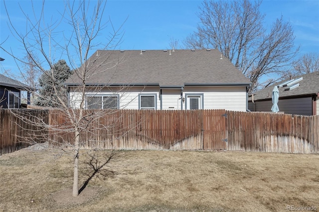 rear view of property with roof with shingles, a yard, and fence