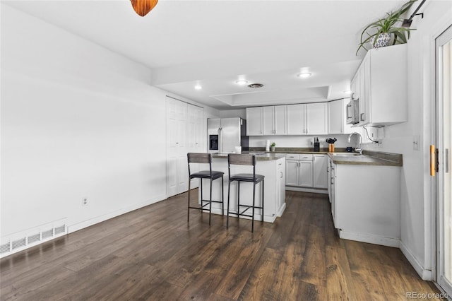 9044 E Nassau Ave, Denver, CO 80237 - kitchen featuring stainless steel appliances, a kitchen breakfast bar, dark wood finished floors, a center island, and white cabinets