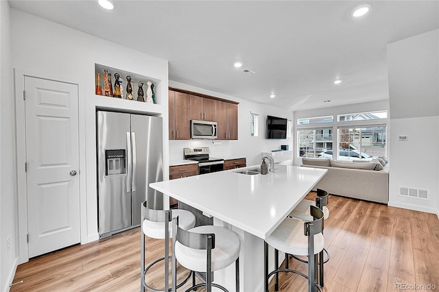 kitchen with appliances with stainless steel finishes, sink, a kitchen breakfast bar, a kitchen island with sink, and light hardwood / wood-style floors