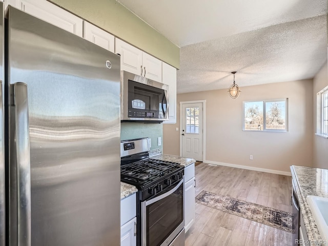 kitchen with sink, white cabinets, light hardwood / wood-style flooring, hanging light fixtures, and appliances with stainless steel finishes