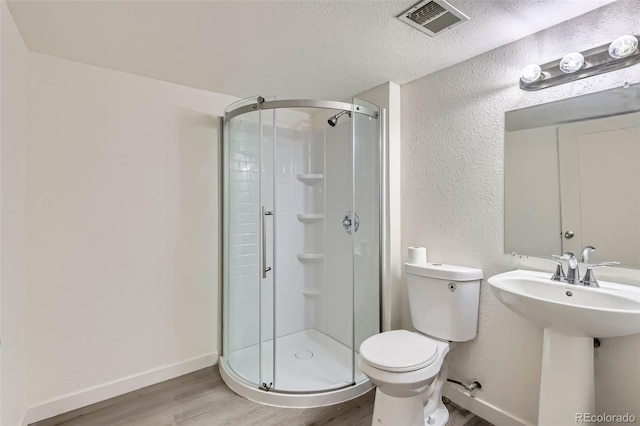 bathroom featuring toilet, an enclosed shower, a textured ceiling, and hardwood / wood-style floors