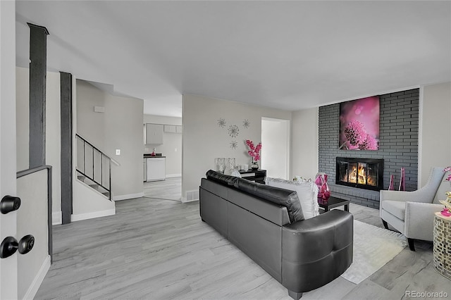 living room with a fireplace, light wood-style flooring, stairs, and baseboards