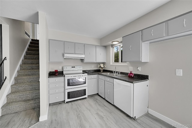 kitchen featuring white appliances, under cabinet range hood, a sink, dark countertops, and gray cabinetry