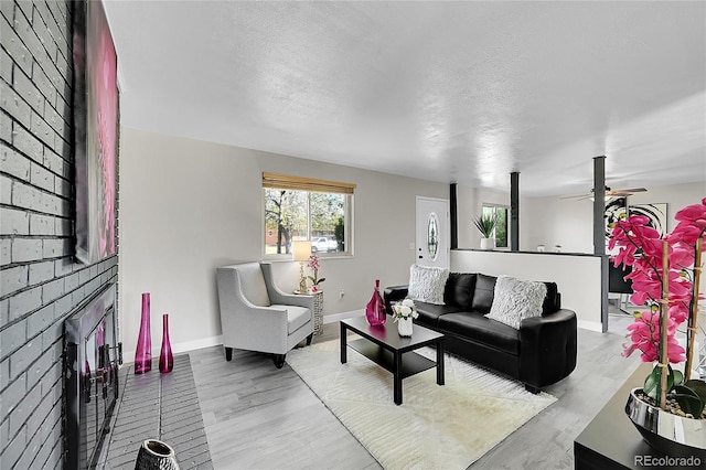 living area with baseboards, wood finished floors, ceiling fan, a textured ceiling, and a brick fireplace