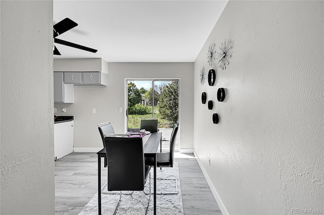 dining area featuring a textured wall, light wood finished floors, baseboards, and a ceiling fan
