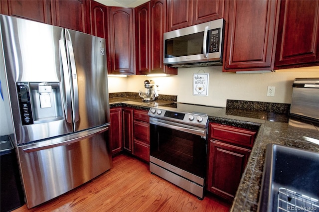 kitchen featuring dark stone countertops, stainless steel appliances, and light wood-type flooring