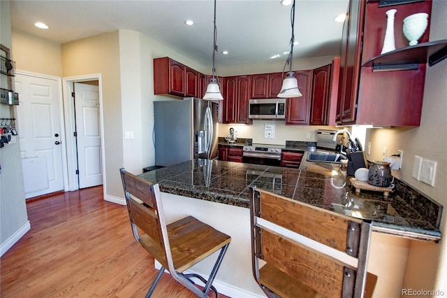 kitchen with sink, hanging light fixtures, stainless steel appliances, kitchen peninsula, and light wood-type flooring