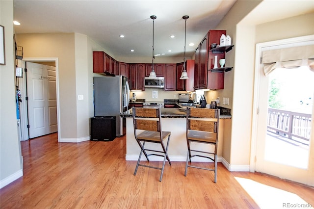 kitchen with stainless steel appliances, hanging light fixtures, a kitchen bar, and light hardwood / wood-style flooring