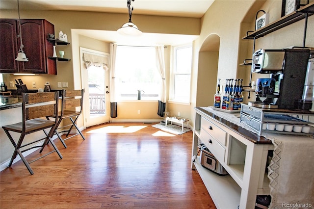 kitchen featuring light hardwood / wood-style flooring, decorative light fixtures, a wealth of natural light, and dark brown cabinets