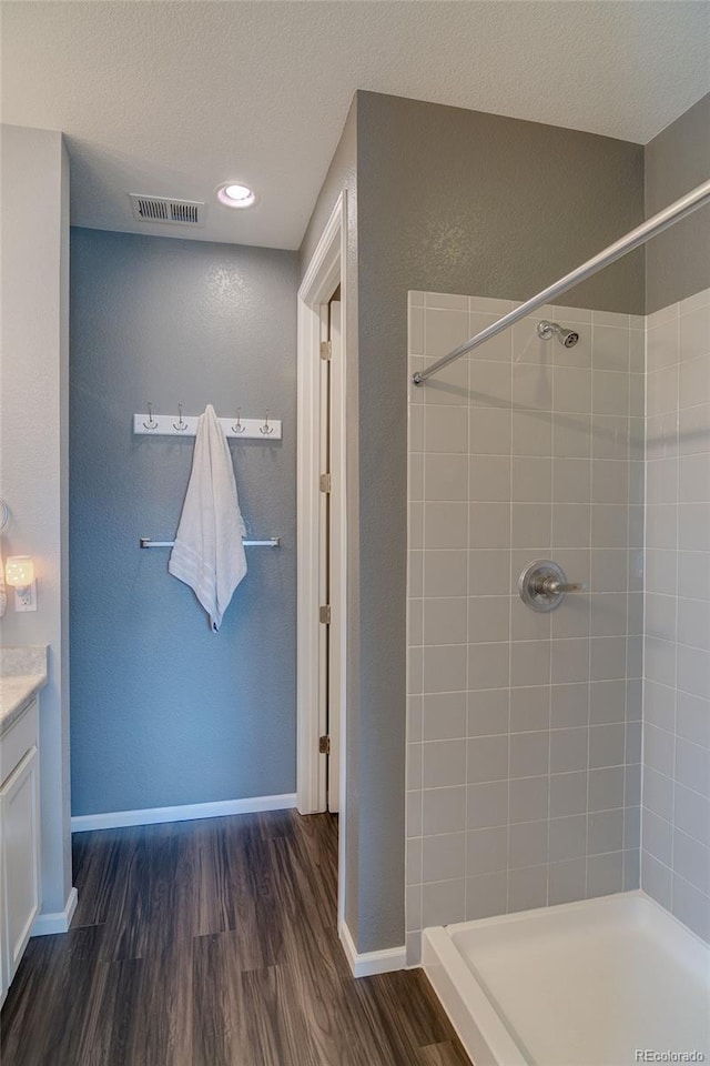 bathroom featuring wood finished floors, tiled shower, baseboards, vanity, and a textured ceiling