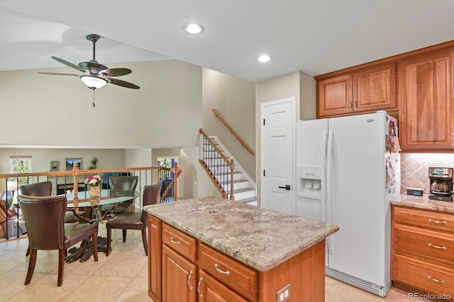 2146 S Ellis Ct, Lakewood, CO 80228 - kitchen featuring white refrigerator with ice dispenser, ceiling fan, brown cabinetry, a center island, and light stone countertops