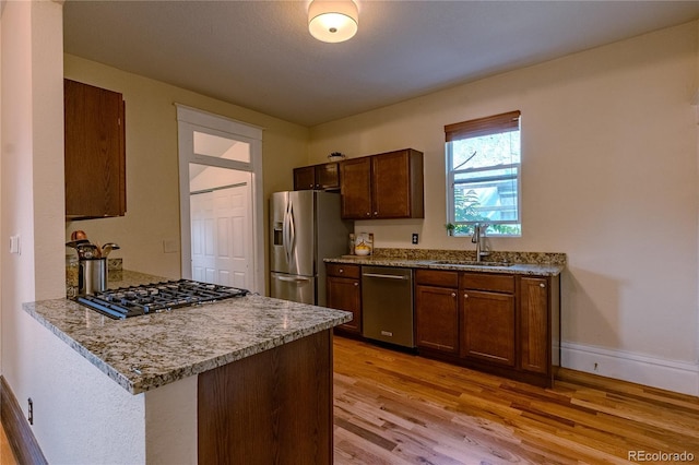 131 Fox St, Denver, CO 80223 - kitchen featuring appliances with stainless steel finishes, light wood finished floors, light stone countertops, and a peninsula