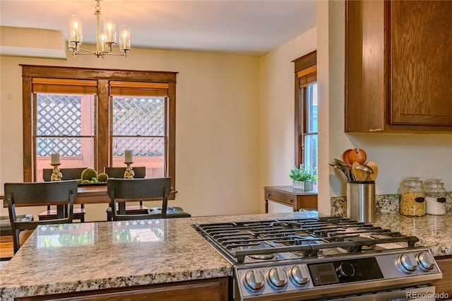 131 Fox St, Denver, CO 80223 - kitchen with stainless steel gas range, a chandelier, light stone countertops, decorative light fixtures, and brown cabinetry