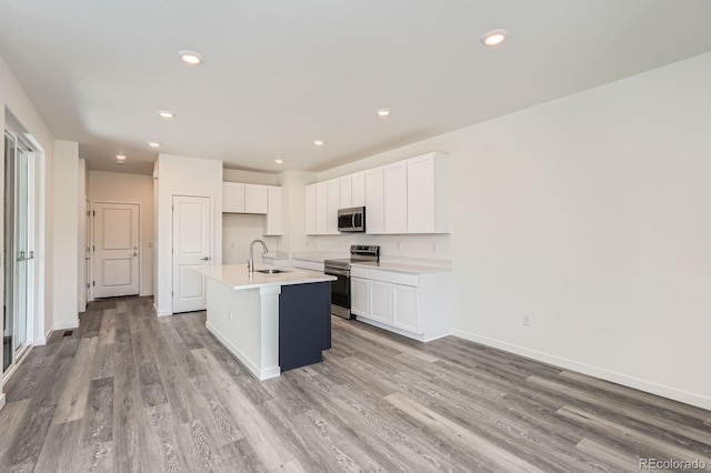 1290 S Algonquian St, Aurora, CO 80018 - kitchen featuring appliances with stainless steel finishes, a sink, light wood-type flooring, white cabinets, and an island with sink