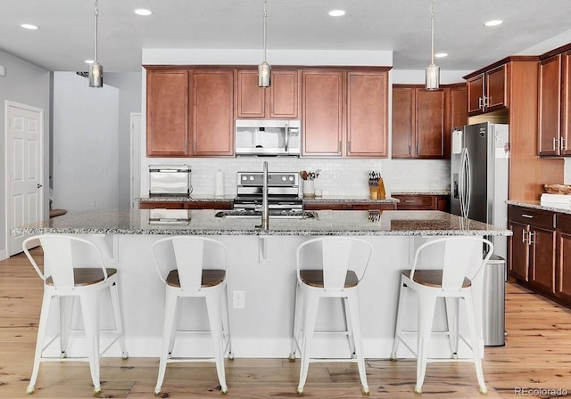 kitchen with a center island with sink, decorative light fixtures, stainless steel appliances, and light hardwood / wood-style flooring