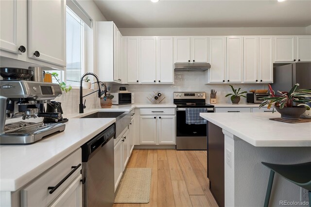 6099 N Netherland Ct, Aurora, CO 80019 - kitchen featuring stainless steel appliances, under cabinet range hood, light countertops, white cabinetry, and tasteful backsplash