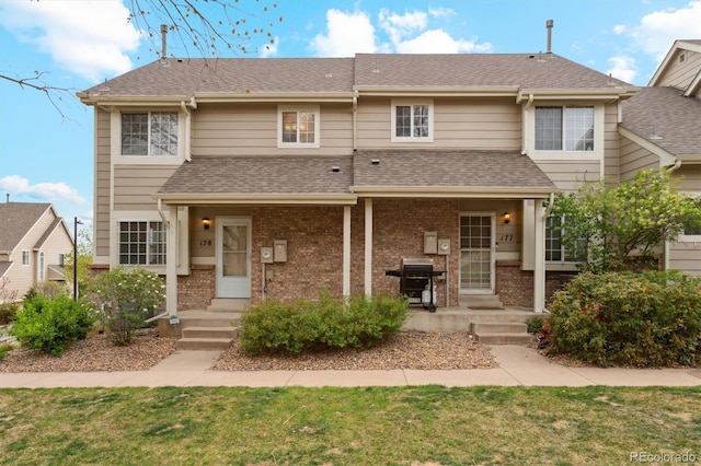 multi unit property with brick siding, a shingled roof, and a front yard