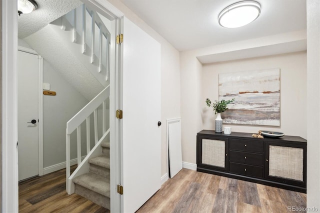 hallway featuring baseboards, wood finished floors, and stairway
