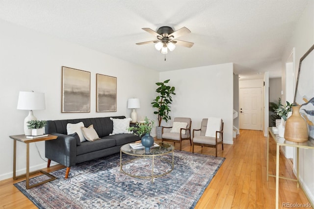 living area with light wood-type flooring, a ceiling fan, baseboards, and a textured ceiling