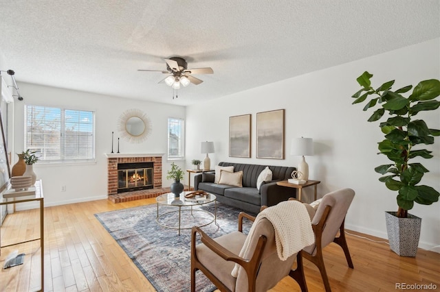 living area featuring a fireplace, baseboards, light wood-type flooring, a textured ceiling, and a ceiling fan