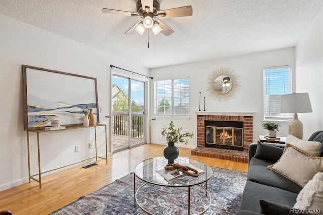 living room with a ceiling fan, a brick fireplace, a textured ceiling, and wood finished floors