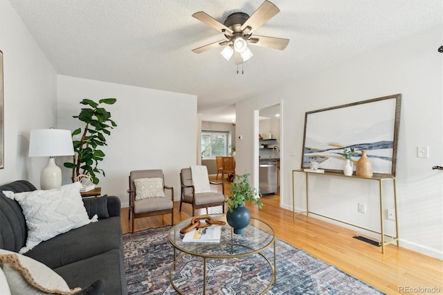living room with a textured ceiling, ceiling fan, visible vents, and wood finished floors