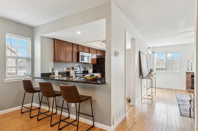 kitchen featuring dark countertops, light wood-style floors, a breakfast bar area, stainless steel microwave, and a sink