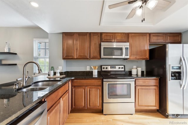 kitchen with ceiling fan, dark stone counters, brown cabinets, a sink, and stainless steel appliances