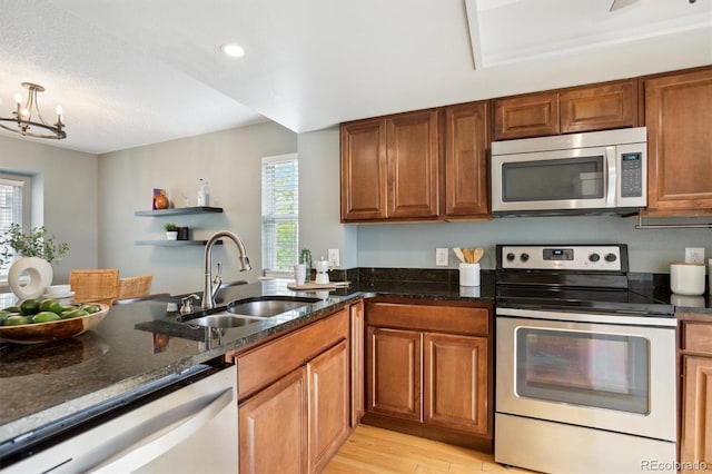 kitchen with appliances with stainless steel finishes, a sink, brown cabinetry, light wood-style flooring, and dark stone countertops