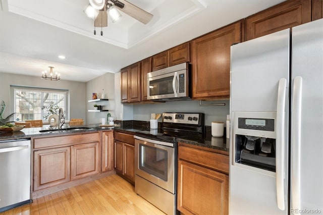 kitchen with appliances with stainless steel finishes, a sink, a raised ceiling, light wood-style floors, and brown cabinetry