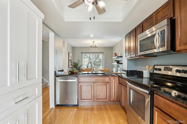 kitchen featuring a sink, appliances with stainless steel finishes, light wood-style floors, and a raised ceiling