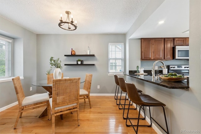 dining room featuring light wood-style floors, baseboards, a textured ceiling, and a chandelier