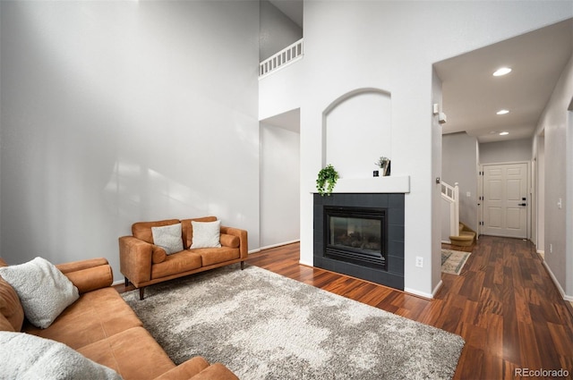 living room featuring a towering ceiling, dark hardwood / wood-style flooring, and a tiled fireplace