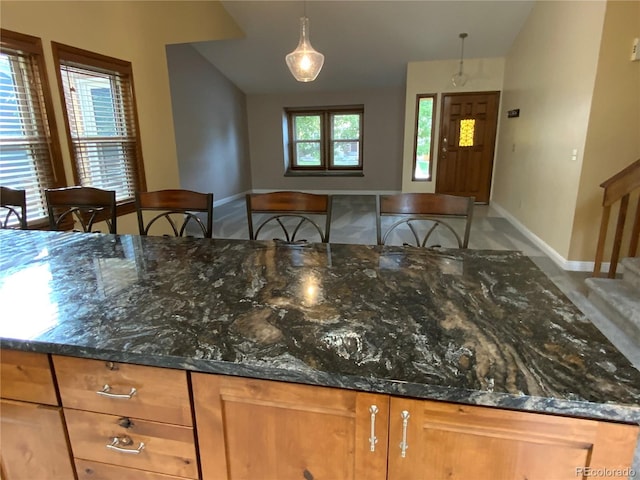 kitchen with a breakfast bar, dark stone countertops, and hanging light fixtures