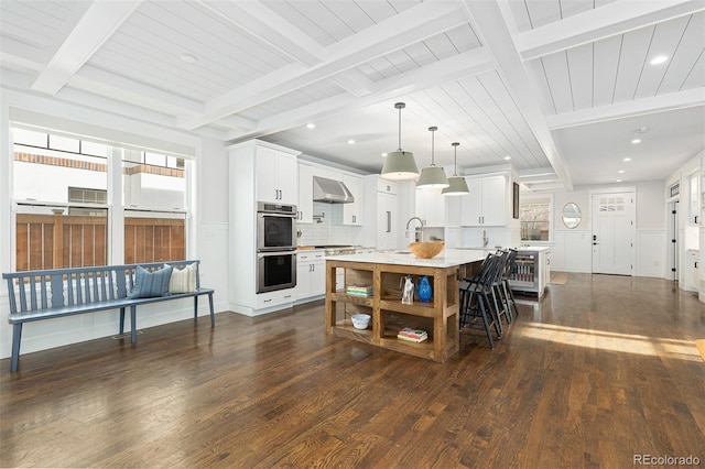 kitchen featuring white cabinetry, wall chimney range hood, pendant lighting, and a center island with sink