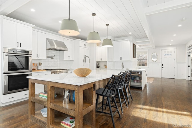 kitchen with a kitchen island, pendant lighting, white cabinets, stainless steel double oven, and wall chimney range hood