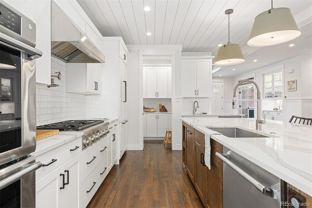 kitchen with white cabinetry, decorative light fixtures, stainless steel appliances, and wall chimney exhaust hood