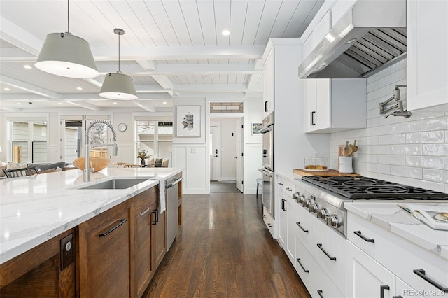 kitchen with light stone countertops, appliances with stainless steel finishes, wall chimney range hood, and white cabinets