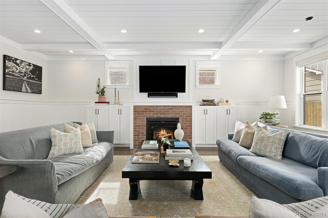 living room featuring beam ceiling, a brick fireplace, and light wood-type flooring