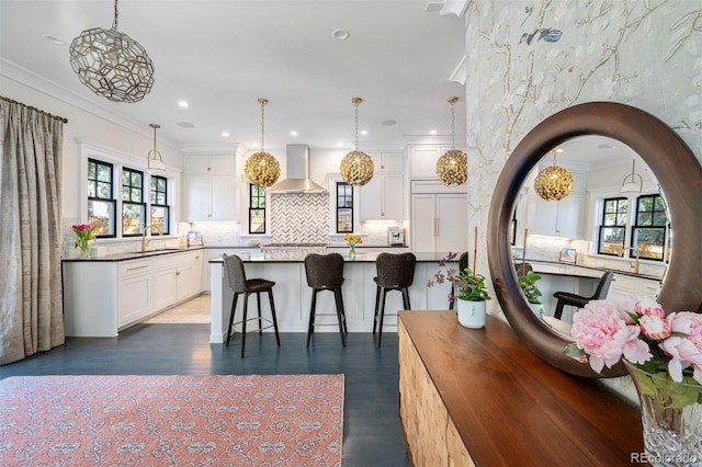 kitchen with sink, white cabinets, wall chimney range hood, decorative light fixtures, and ornamental molding