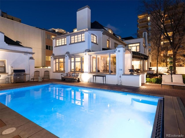 pool at night with a patio, grilling area, an outdoor bar, and exterior kitchen